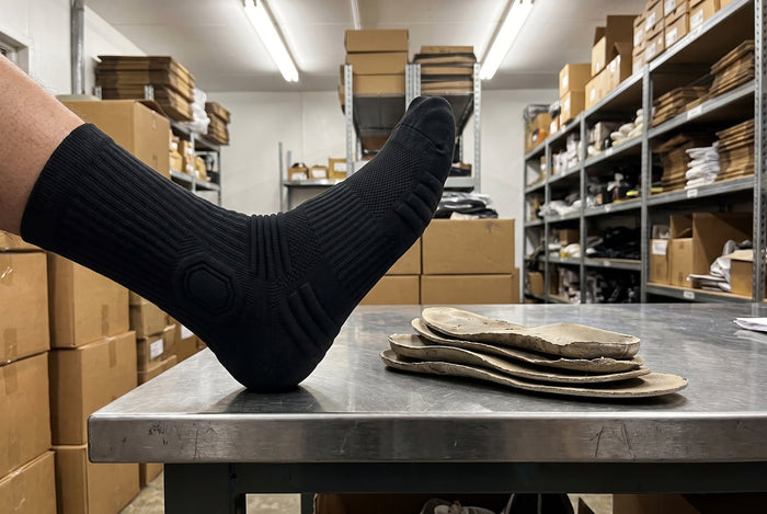 Chaussette HARDSEN posée sur une table de réserve, à côté de semelles usées